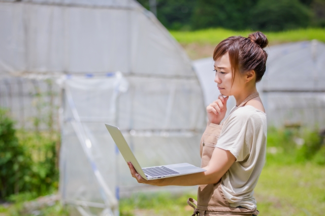 ノートパソコンを見ながら考える農家の女性